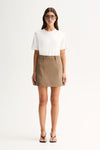 A woman modeling a white short-sleeve crewneck t-shirt and a brown mini skirt with a matching belt, paired with black thong sandals, against a plain white studio background.