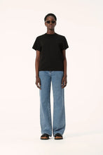 Model wearing the black Zoe Tee with light blue straight-leg jeans, black sandals and sunglasses, showing the crew neckline, short sleeves and slightly oversized boxy fit, full-length front view
