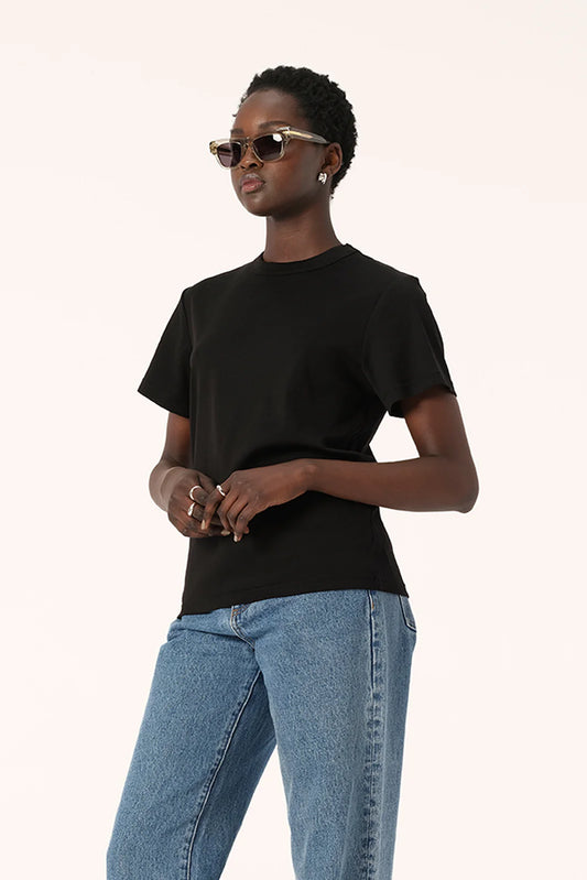Model wearing the black Zoe Tee with light blue jeans and sunglasses, showing the relaxed boxy silhouette, short sleeves and crew neckline, upper-body angled view

