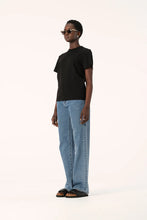 Model wearing the black Zoe Tee with light blue jeans and black sandals, showing the straight hem, relaxed fit and short sleeves, full-length side angled view
