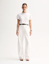 A model wearing a white relaxed-fit T-shirt with a round neckline and short sleeves, tucked into white straight-leg trousers with a black belt and black flat sandals.