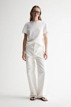 Model wearing the white Zoe Tee with white relaxed trousers, sunglasses and flat sandals, showing the crew neckline, short sleeves and slightly oversized boxy fit, full-length front view
