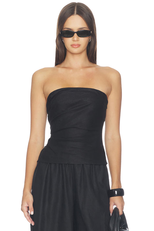 Front view of the model wearing the black strapless top, showing the straight neckline, fitted silhouette, diagonal fabric draping across the bodice and flared hem over matching black trousers.
