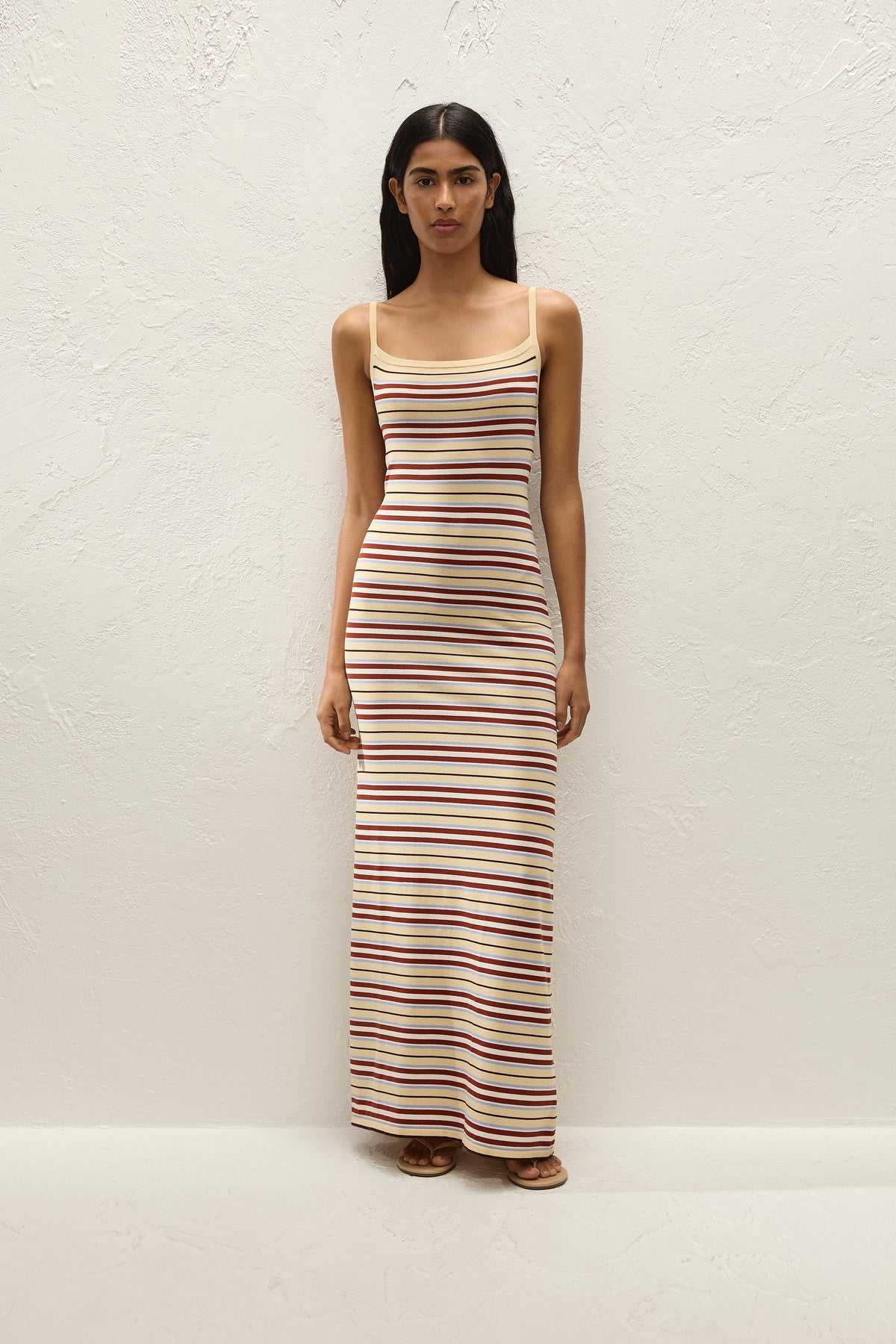 Full-length front view of the striped maxi dress styled with flat sandals against a textured cream wall.