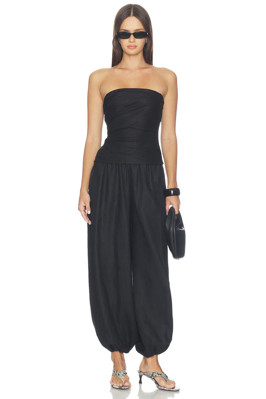 Model wearing black balloon pants with a black strapless top, narrow black sunglasses, a black clutch and snakeskin-patterned heeled sandals, showing the voluminous legs and gathered ankle hems.