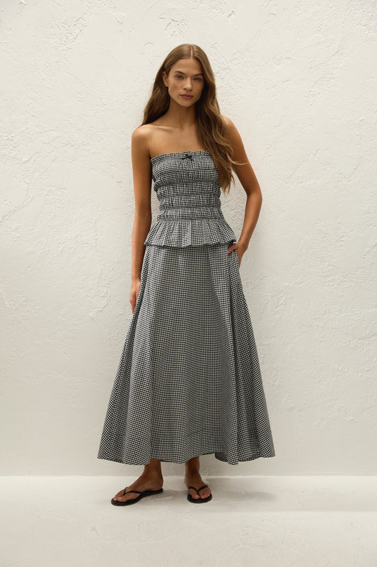 A woman wears a black and white gingham midi skirt with a matching strapless top and black sandals.
