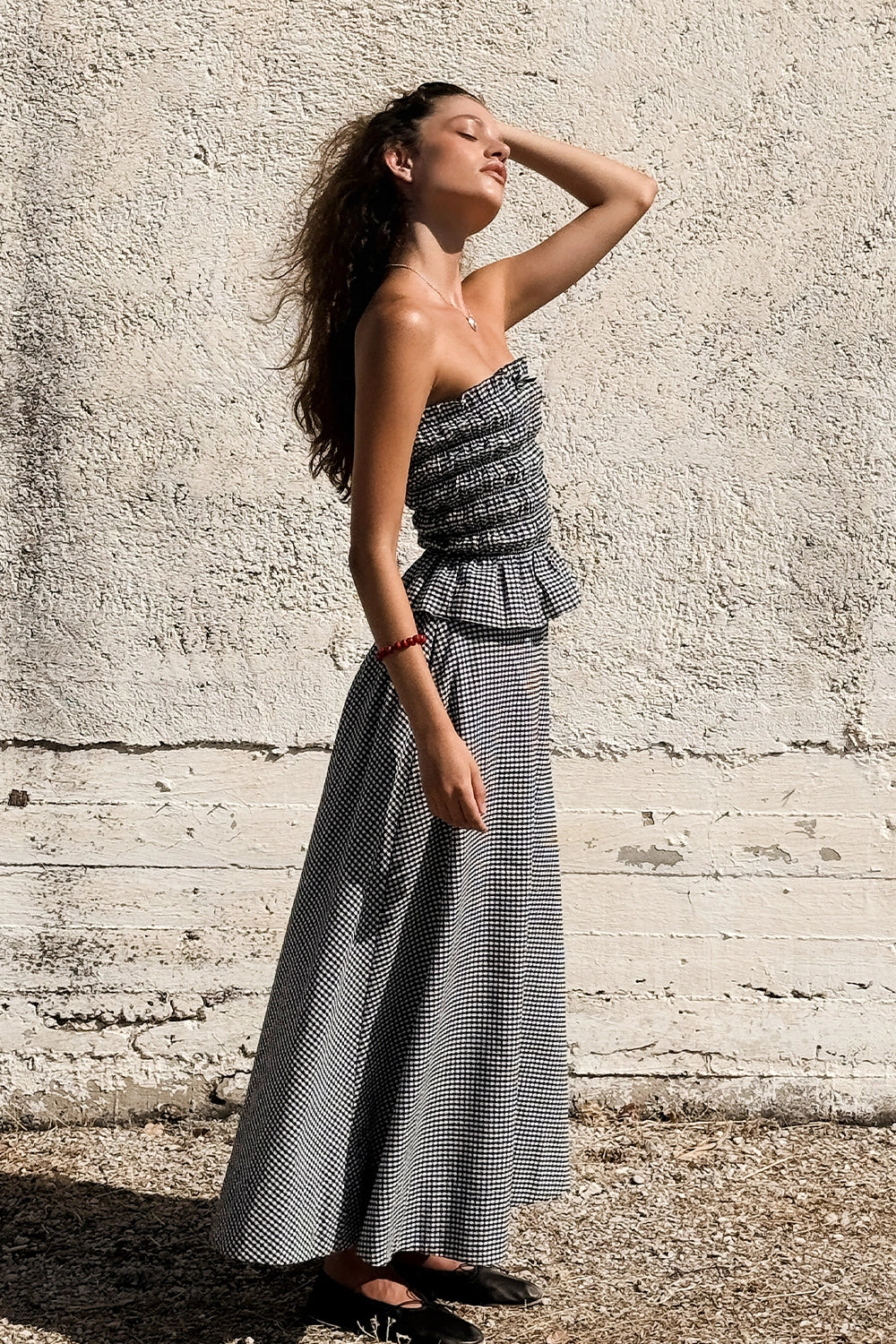 A woman wears a black and white gingham midi skirt outdoors against a textured wall.
