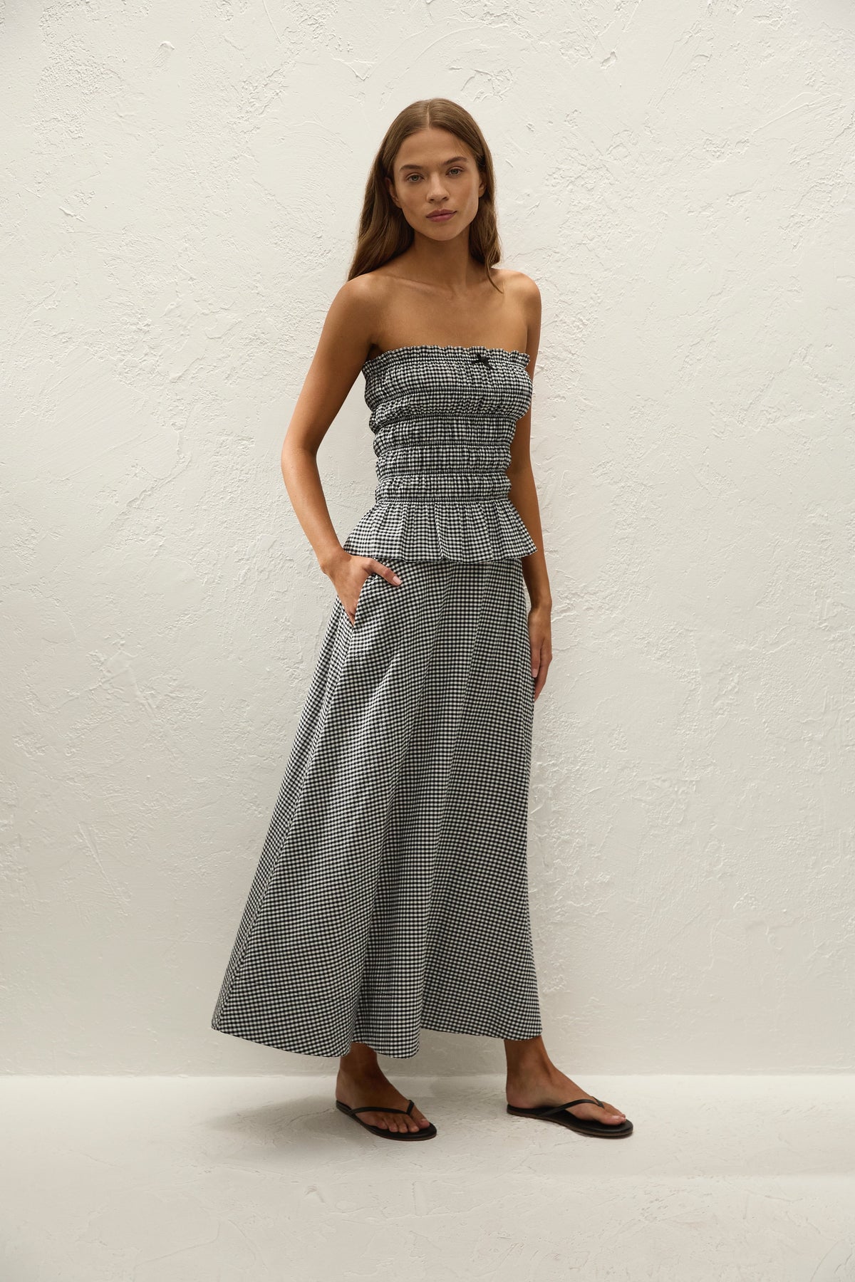 A woman wears a black and white gingham midi skirt with a matching strapless top in a full-length front view.
