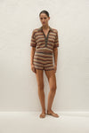 Full-length front view of the striped knit polo styled with matching shorts and neutral sandals against a textured cream wall.