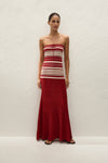 A woman wears a red and cream striped strapless maxi dress with a long pleated red skirt.
