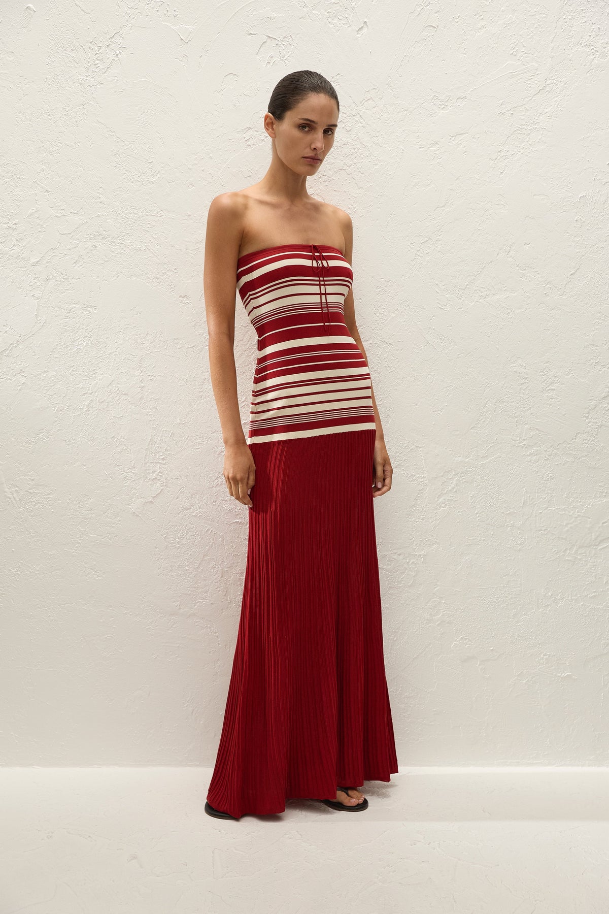 A woman wears the red and cream strapless maxi dress in a full-length angled front view.
