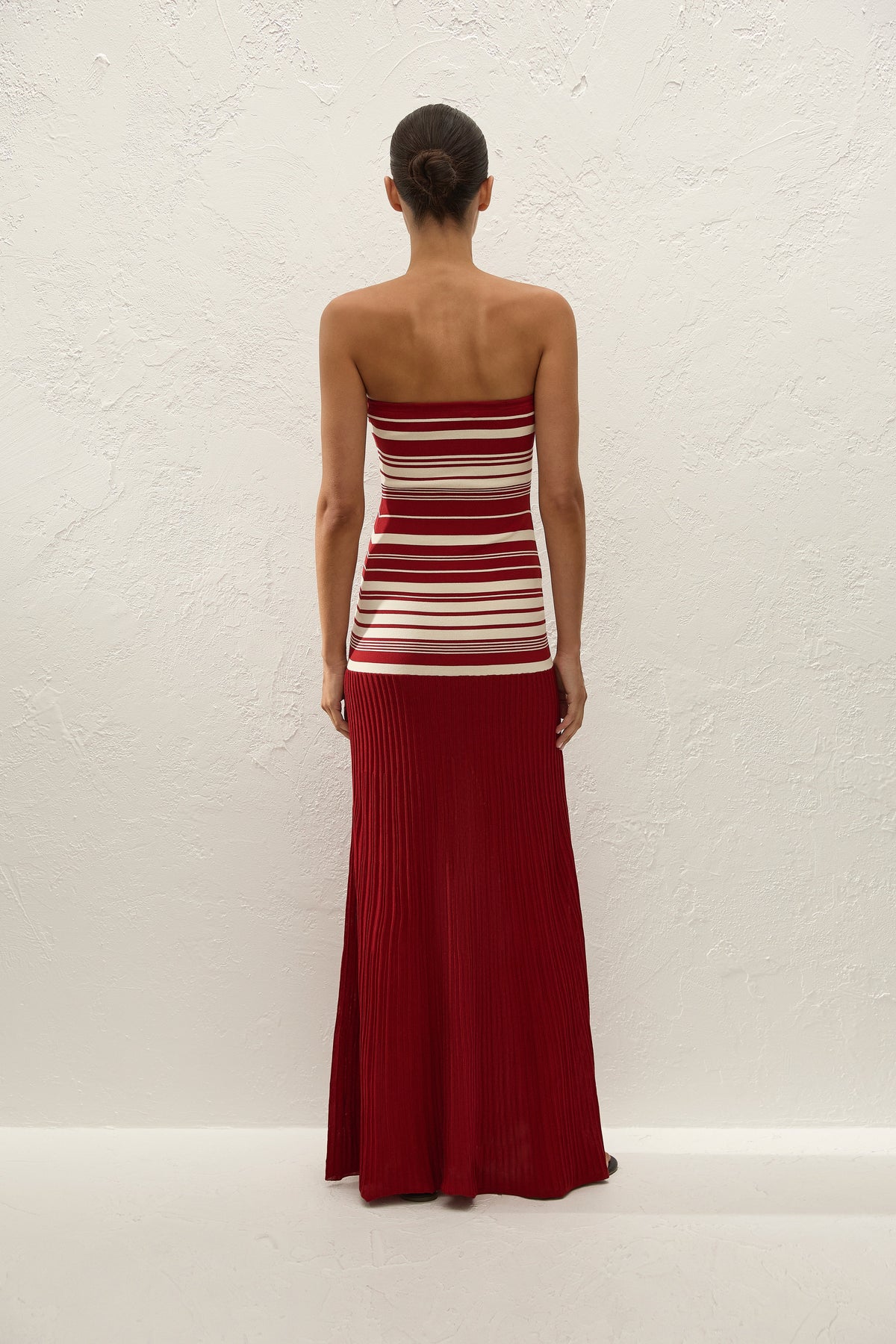 A woman wears the red and cream strapless maxi dress in a full-length back view.
