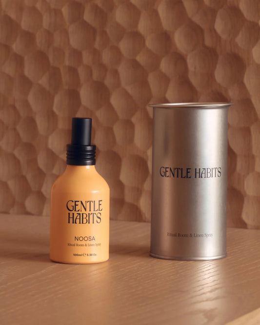 Noosa room and linen spray shown beside its cylindrical metal container on a wooden surface.