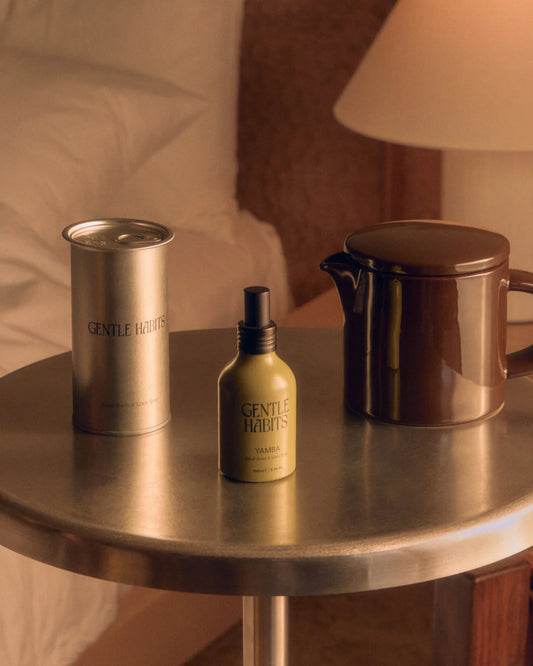 Gentle Habits Ritual Room & Linen Spray in Yamba shown beside its cylindrical metal container on a wooden surface.