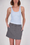 A woman wearing a pale blue ribbed tank top with a scoop neckline and wide shoulder straps, paired with a black-and-white checked mini skirt, photographed from the front with her hands in the skirt pockets.