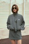  A model poses outdoors in a black and white check bomber jacket and matching mini skort, showing the jacket's relaxed silhouette, high neckline and coordinated check pattern.