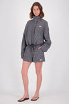 Full-length view of a model wearing a black and white check bomber jacket with a high collar and gathered drawstring hem, paired with matching check shorts and flat sandals.