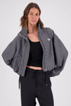 A model wears an open black and white check bomber jacket over a black cropped top and black drawstring trousers, showing the front zip, high collar, voluminous sleeves and relaxed cropped shape.