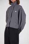 Close-up of a black and white check bomber jacket showing the raised collar, front zip fastening, chest logo embroidery and vertical front pocket.