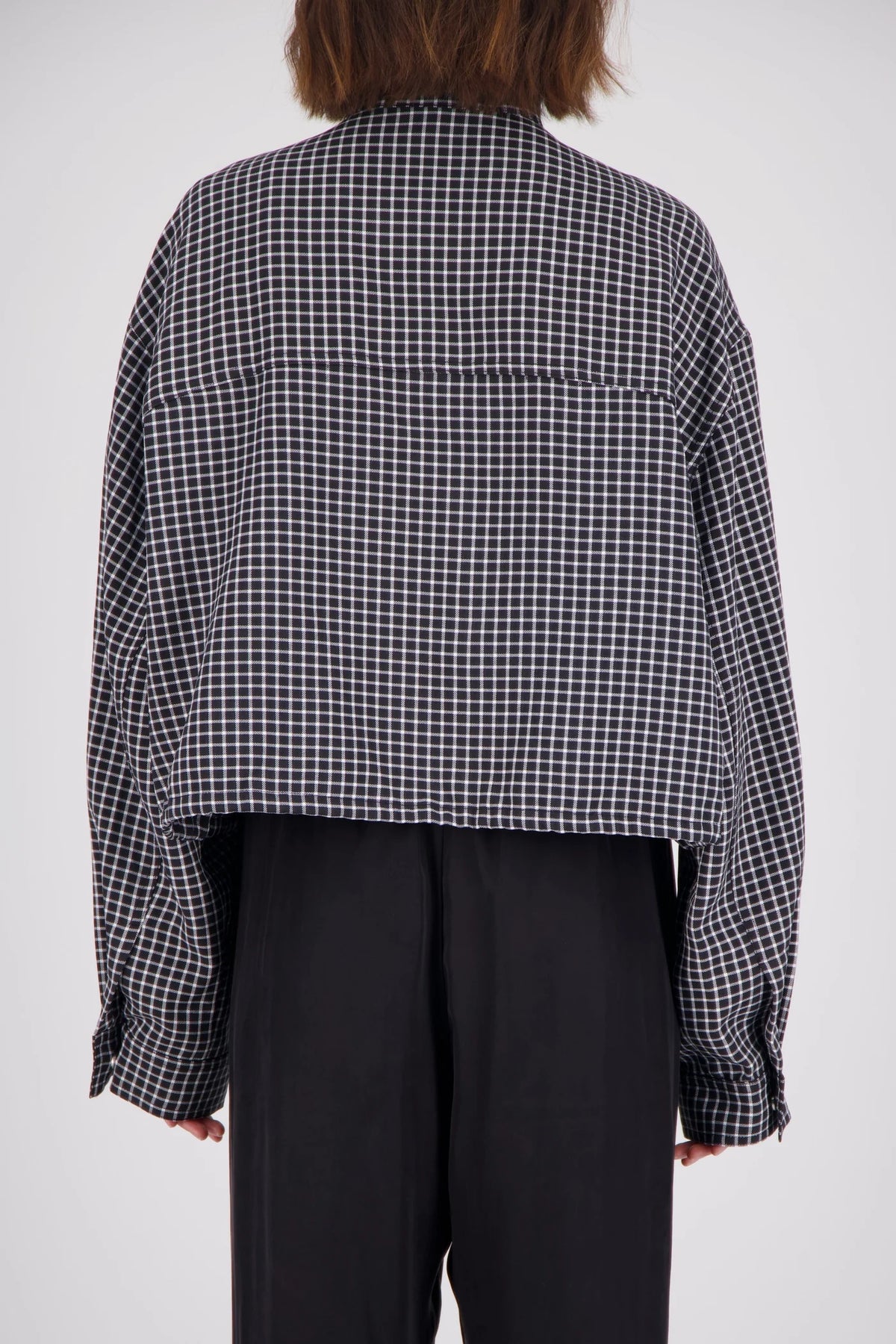Rear view of a black and white check bomber jacket showing the all-over grid pattern, loose-fitting sleeves, back panel seams and gathered hem.
