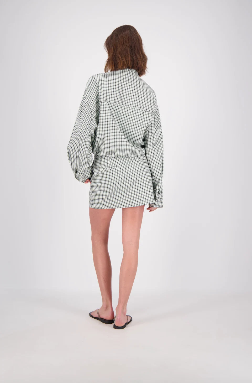 A rear view of the white and mint check bomber jacket, showing the all-over grid pattern, loose long sleeves, back yoke seam and cropped hem.
