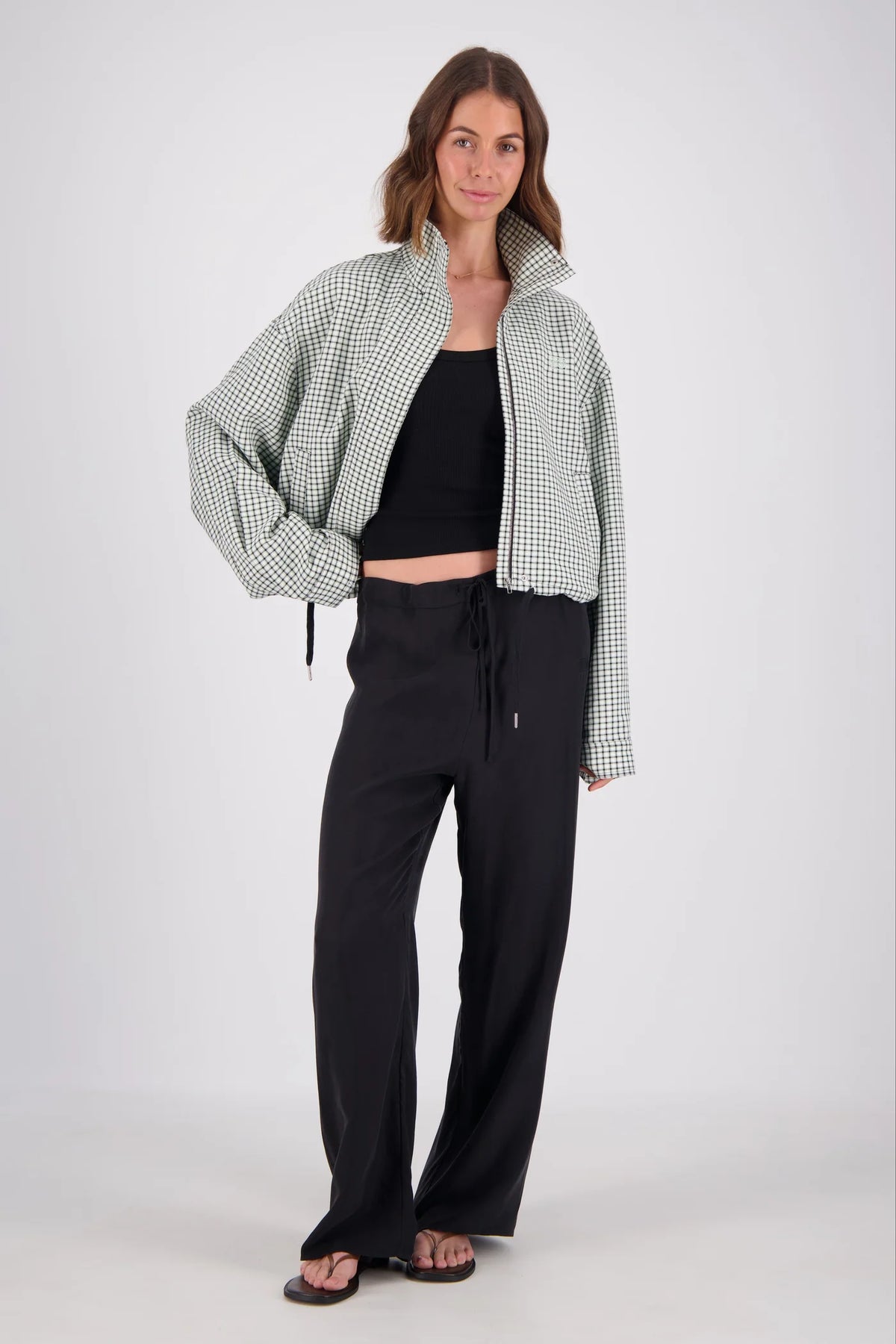 A close front view of the white and mint check bomber jacket, highlighting the high collar, front zip fastening, side pocket opening and small embroidered chest emblem.