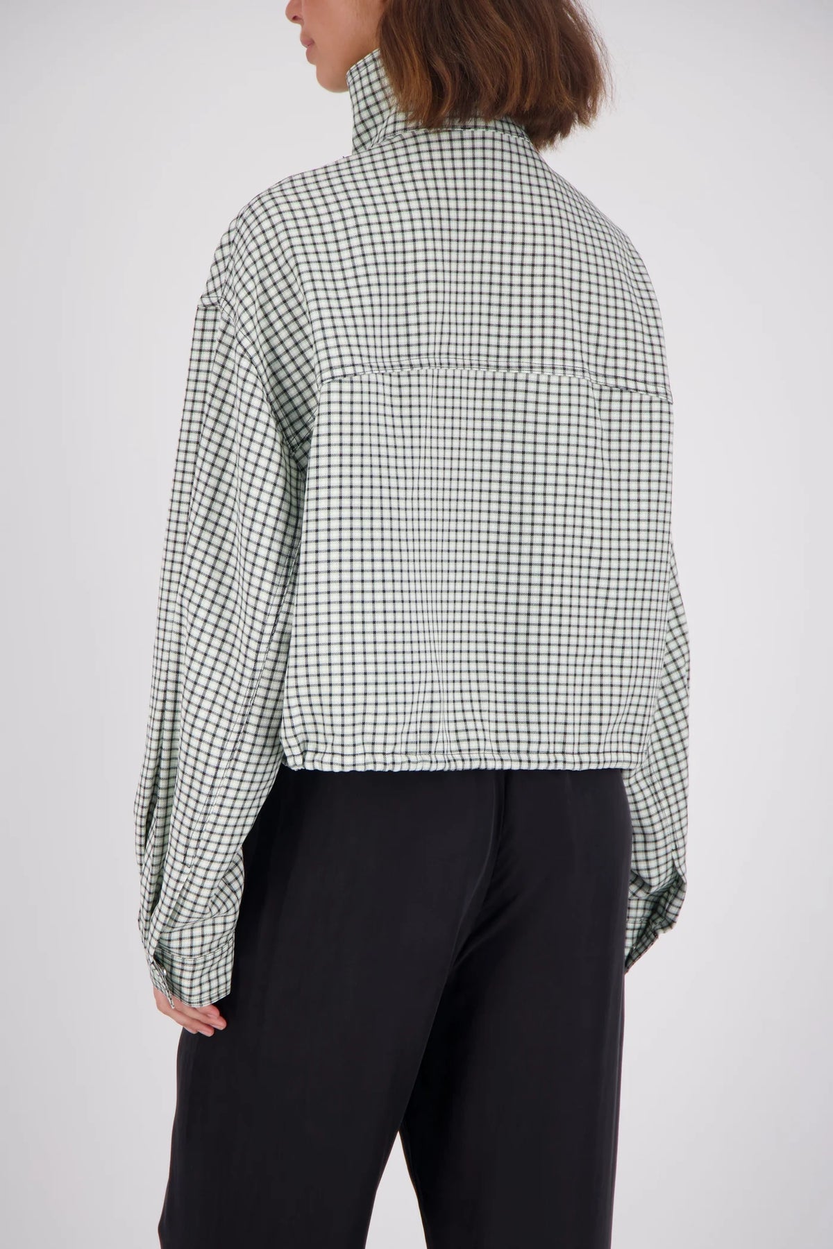 A rear studio view of the white and mint check bomber jacket, displaying the all-over grid pattern, back yoke seam, loose sleeves and cropped hem.