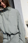 A close-up outdoor view of the white and mint check bomber jacket, highlighting the fine grid pattern, raised collar, front fastening and small embroidered chest emblem.