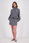 Front view of a model wearing the black and white check mini skort with a pale blue sleeveless tank top, showing the high waistband, belt loops, front pockets and concealed front closure.