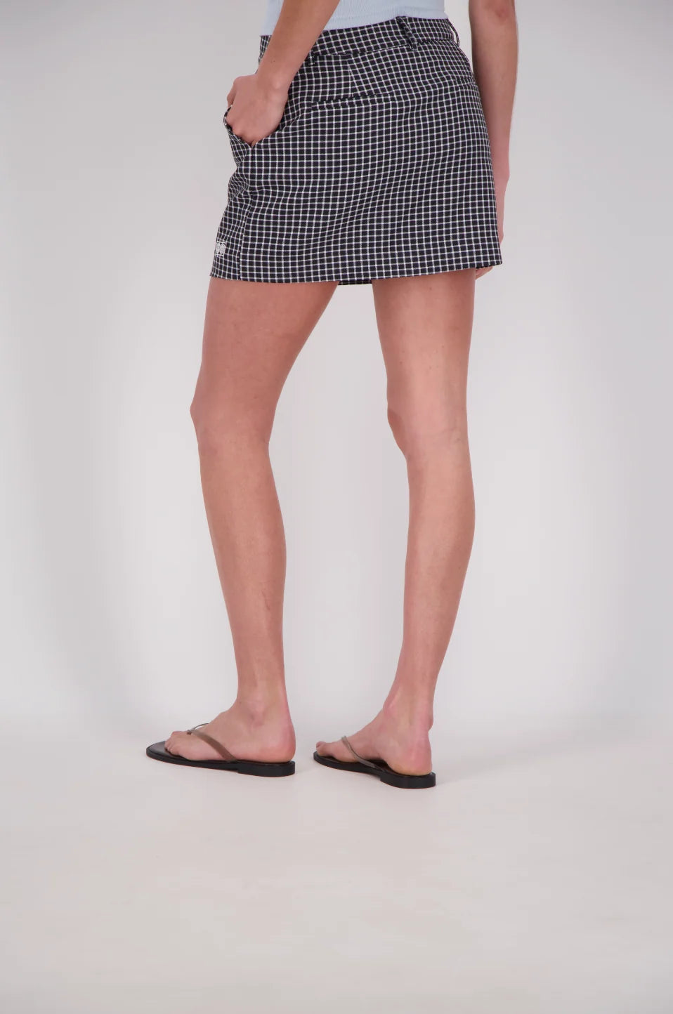 Rear three-quarter close-up of a black and white check mini skort, showing the fitted waistband, belt loops, back welt pockets and straight hem above the thighs.