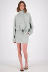 A woman modelling a white and mint checked outfit with a high-neck zip jacket and matching mini skort, photographed from the front in a studio.