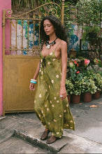 Woman in a green polka dot dress standing in front of a colorful wall and plants.