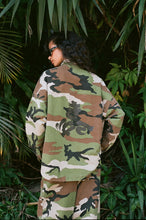 Person wearing a camouflage jacket standing among green foliage