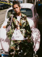 Person wearing a camouflage outfit standing in front of a vintage car.