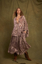 A model wears the purple metallic floral shirred maxi skirt with a matching oversized shirt and brown boots against an olive studio backdrop.