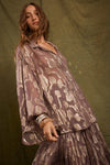 Model wearing the purple Collector Chalm Shirt with a metallic floral pattern and relaxed button-through silhouette against an olive backdrop.
