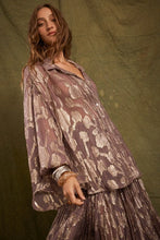Model wearing the purple Collector Chalm Shirt with a metallic floral pattern and relaxed button-through silhouette against an olive backdrop.