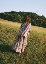 Model wearing the purple metallic floral shirt with the matching skirt in an outdoor field, highlighting the fluid oversized silhouette.