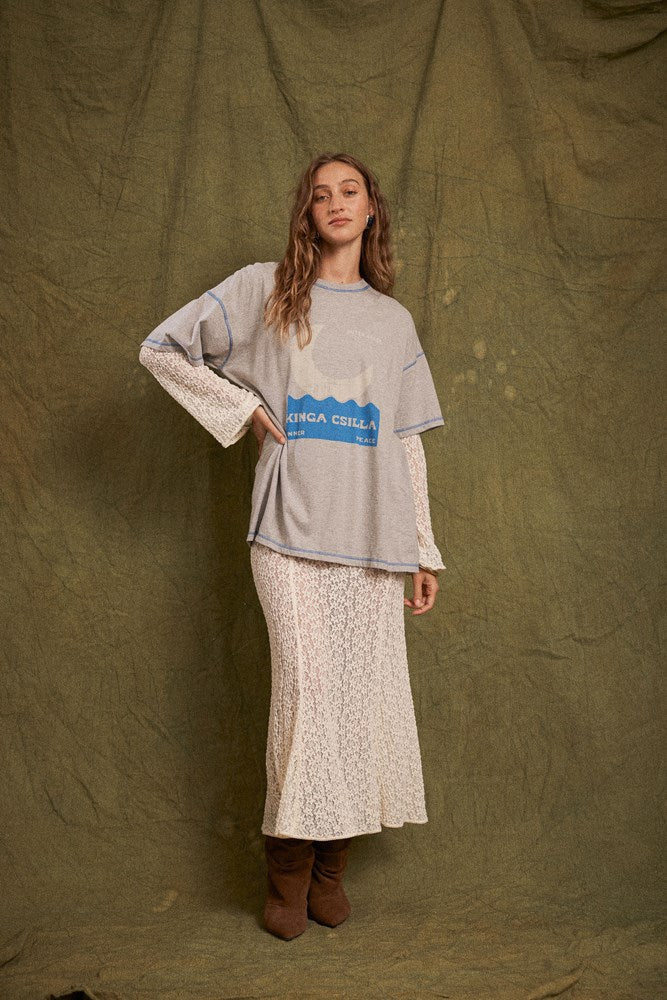 Model wearing the grey marl Inner Peace graphic tee layered over cream lace sleeves with a matching lace maxi skirt and brown boots in a full-length front view.
