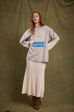 Model wearing the oversized grey marl graphic tee with cream lace layers and brown boots, showing the relaxed fit, blue contrast stitching and front artwork.