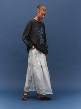 Model wearing a vintage black long-sleeve graphic tee with a light grey maxi skirt and black flats, showing the relaxed oversized silhouette and sleeve graphics, angled front view