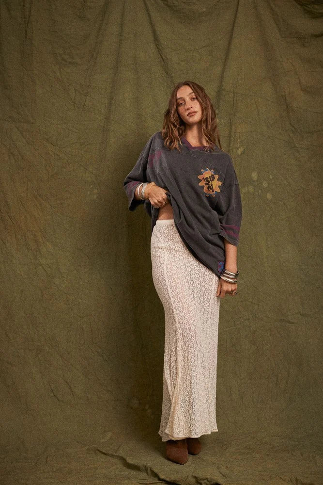 Model wearing the cream lace maxi skirt with an oversized charcoal graphic tee and brown ankle boots, showing the fitted waist, flowing length and softly flared lace silhouette in a full-length front view.