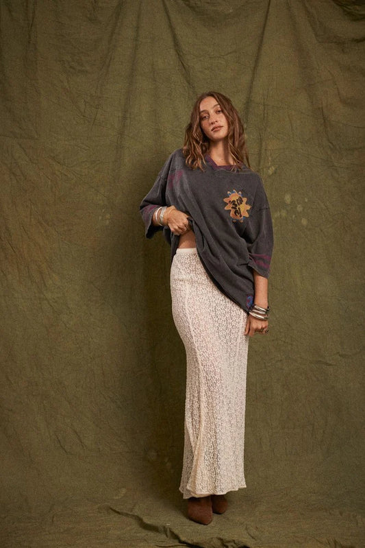 Model wearing the cream lace maxi skirt with an oversized charcoal graphic tee and brown ankle boots, showing the fitted waist, flowing length and softly flared lace silhouette in a full-length front view.