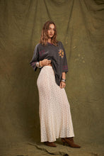 Model wearing the cream lace maxi skirt with an oversized graphic tee and brown ankle boots, showing the long flowing shape, delicate lace texture and gently flared hem in an angled front view.