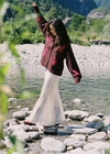 Model wearing the cream lace maxi skirt with a brown cardigan beside a mountain lake, showing the flowing maxi length, softly flared hem and delicate lace finish in a lifestyle front view.