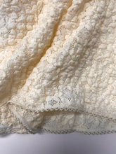 Close-up of the cream lace fabric, showing the intricate floral texture, semi-sheer openwork pattern and delicate contrast edging along the hem.