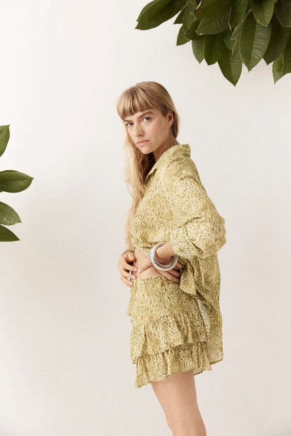 Side view of the Dorato printed button-up shirt styled with matching ruffle shorts and silver bangles against a clean white backdrop with leafy branches.