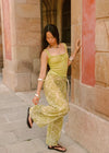 Lifestyle side view of the Dorato printed wide-leg pants styled with a light green tank top and black sandals beside a stone archway.