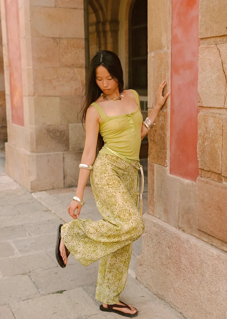 Lifestyle side view of the Dorato printed wide-leg pants styled with a light green tank top and black sandals beside a stone archway.