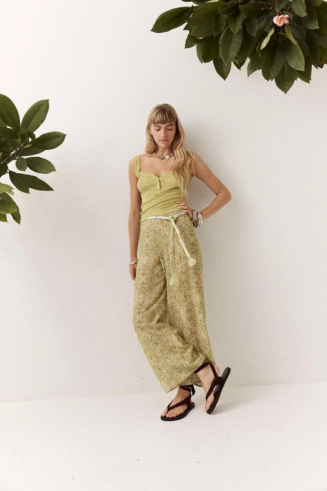 Front angled view of the Dorato printed wide-leg pants with a tasseled waist tie, styled with a light green tank top and black sandals in a white studio setting.